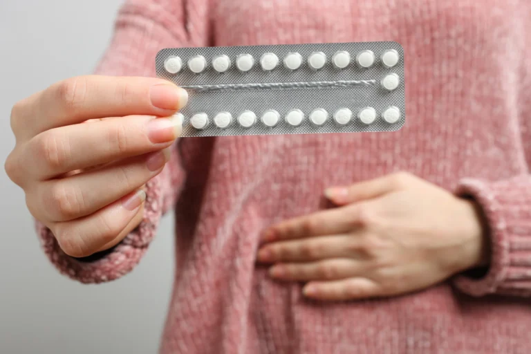 A woman holding a pack of birth control pills with one hand while the other hand is placed on their abdomen, illustrating the use of birth control for managing endometriosis.